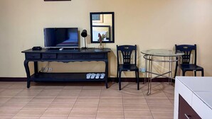 A living room with a TV, a coffee table, two chairs, a small shelf, and a framed picture on the wall. - Poblacion Suites by SMS Hospitality (Makati)