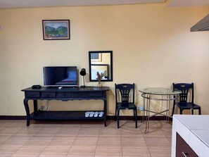 A living room with a TV, a coffee table, two chairs, a small shelf, and a framed picture on the wall. - Poblacion Suites by SMS Hospitality (Makati)