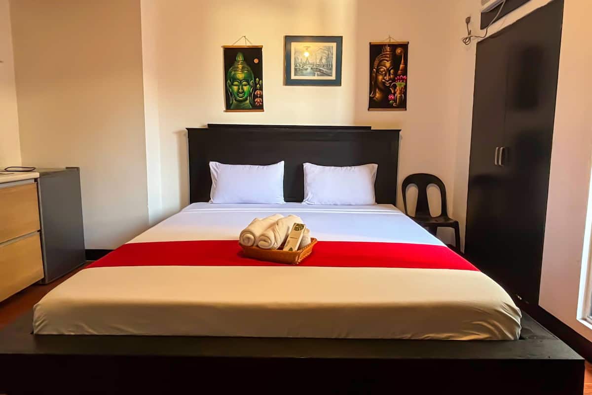 Habitación de hotel con cama, dos cuadros en la pared, un armario y un escritorio con silla.