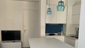 Eine moderne Küche mit weißer Arbeitsplatte, einem Barhocker, einem Fernseher und Pendelleuchten.