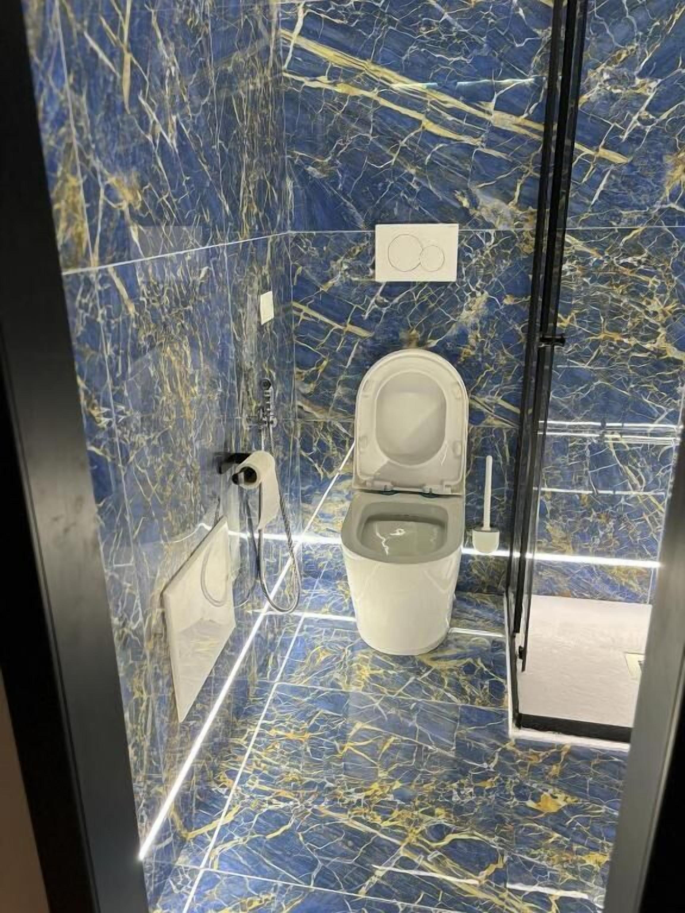 Een badkamer met een marmeren vloer, toilet en douchehoek.