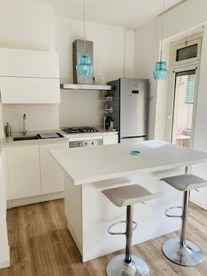 Eine moderne Küche mit weißen Schränken, einem Edelstahlkühlschrank, einem Gasherd und zwei Barhocker.