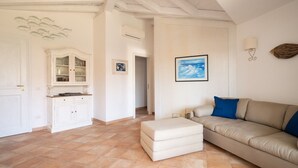 Un salon avec un canapé beige, un petit pouf, une armoire blanche et un tableau encadré au mur.