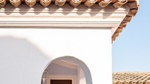 Un bâtiment blanc avec un toit en tuiles, une porte d’entrée en arc de cercle et une porte en bois.