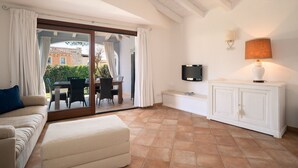 Une pièce comprenant un canapé, une table à manger avec des chaises, un téléviseur, un meuble et une porte-fenêtre coulissante donnant sur un espace extérieur.