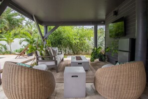 Un área de estar al aire libre con techo, mobiliario de mimbre, un televisor de pantalla plana y una chimenea de piedra.