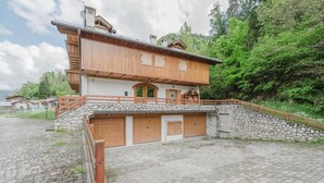 A two-story wooden chalet with a stone foundation, a wooden deck, and a stone wall. - I Folli di Alleghe Apartment - Parking (Caprile)