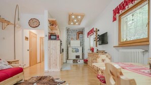 A cozy living room with a wooden sofa, a dining table with chairs, a fireplace, and a television. - I Folli di Alleghe Apartment - Parking (Caprile)