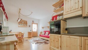 A cozy kitchen with wooden cabinets, a red sofa, and a dining area with chairs and a table. - I Folli di Alleghe Apartment - Parking (Caprile)