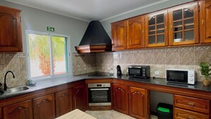 Una cocina con armarios de madera, estufa, microondas y ventana con vista a árboles.