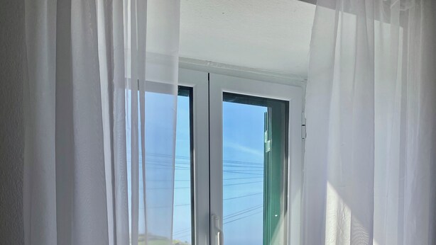 Una ventana con cortinas blancas, vista a un paisaje rural y un marco de puerta verde.