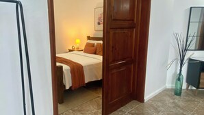 Habitación de hotel con cama, mesita de noche, lámpara, un cuadro en la pared y un jarrón con ramas.