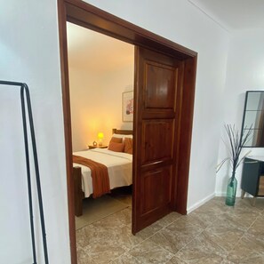 A hotel room with a bed, a nightstand, a lamp, a framed picture on the wall, and a vase with branches. - Cozy Island Suite In an Azorean Village! Large Family Suite with tons of charm. (Remédios)