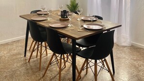 Un comedor con mesa de madera dispuesta para cuatro, sillas negras con patas de madera y un cuadro en la pared.