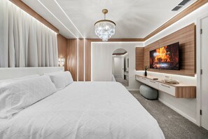 A modern bedroom with a large bed, a TV mounted on the wall, and a chandelier. - 6BR house sleeps 16 with private pool (Kissimmee)