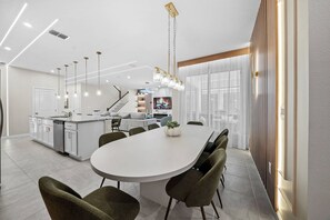 Une cuisine moderne dotée d’un îlot central, d’un coin repas avec une grande table et d’un escalier menant à un niveau supérieur.