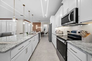 A modern kitchen with white cabinetry, a granite countertop, stainless steel appliances, and pendant lighting. - 6BR house sleeps 16 with private pool (Kissimmee)