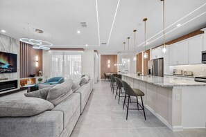 Une cuisine moderne dotée d’un îlot central, de tabourets de bar et d’un coin repas avec une longue table.