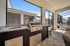 Eine Außenküche mit integriertem Grill, einer Spüle und einem großen Fenster mit Blick auf eine Terrasse.