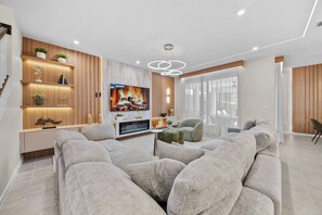 A modern living room with a large sofa, a television, and a fireplace. - 6BR house sleeps 16 with private pool (Kissimmee)