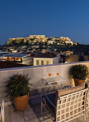 A terrace with a table and chairs, overlooking a historic cityscape with ancient ruins on a hill. - Ergon House Ermou (Athens)