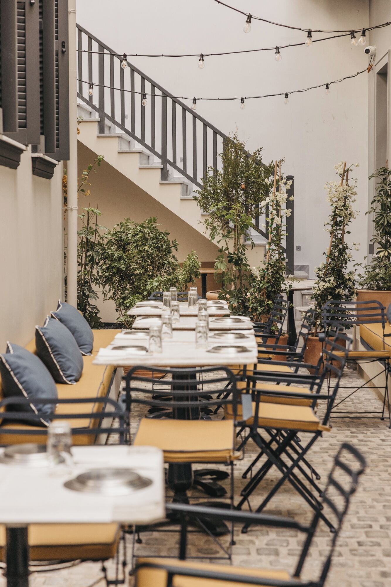An outdoor dining area with tables and chairs, a staircase, and potted plants.