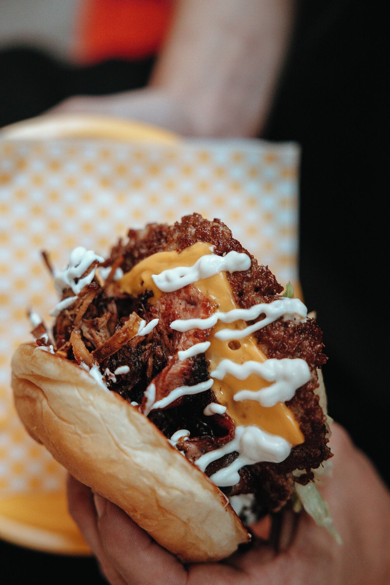 A person holding a sandwich with a bun, meat, cheese, and sauce.