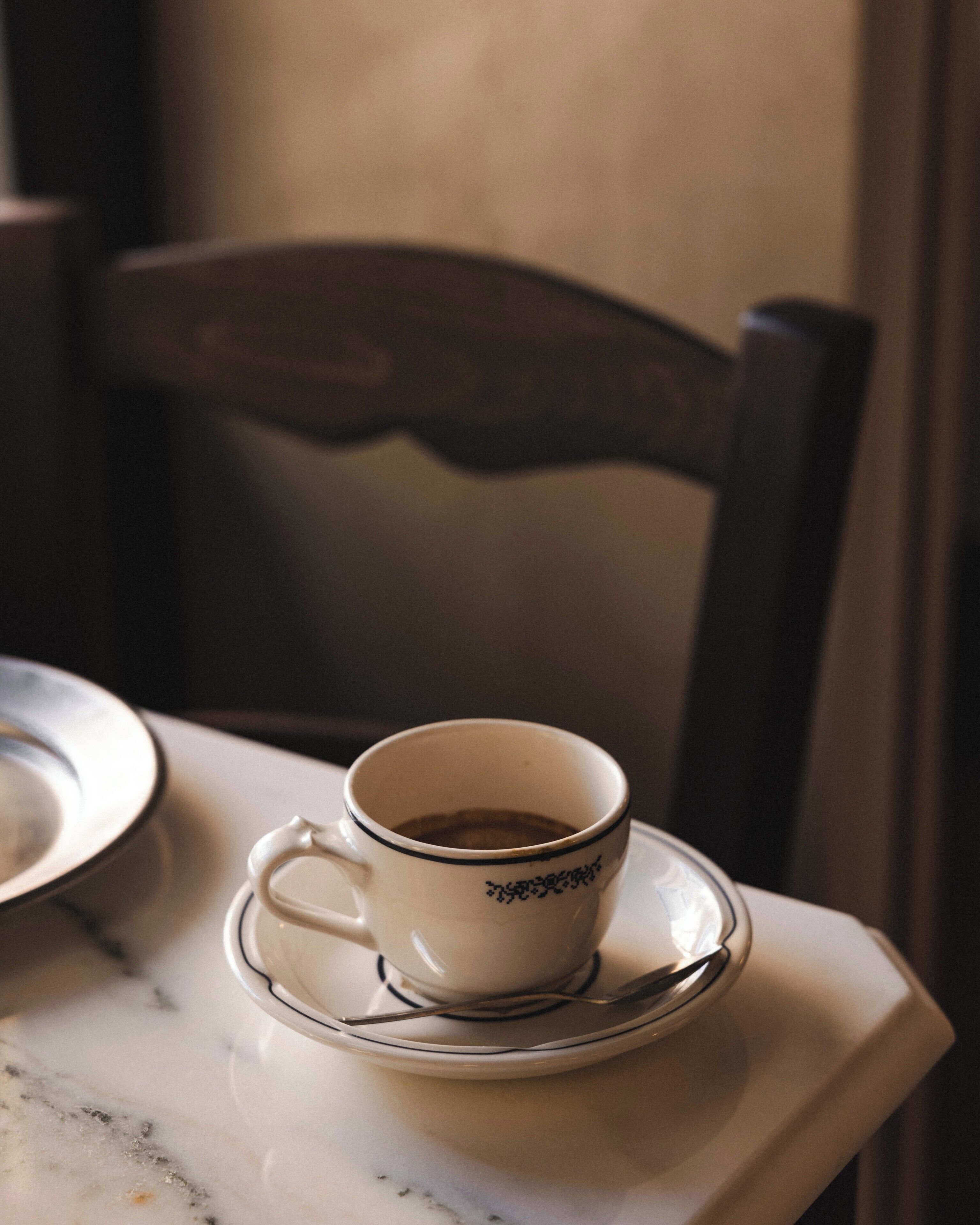 Eine Tasse Kaffee auf einem Untertasse, ein Teller und ein Stuhl.