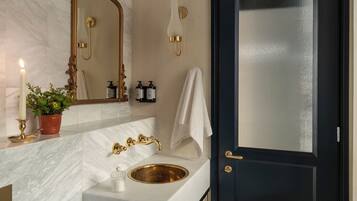 Une salle de bain avec un meuble-lavabo en marbre, des robinetteries dorées, un grand miroir, une porte noire et une plante en pot.