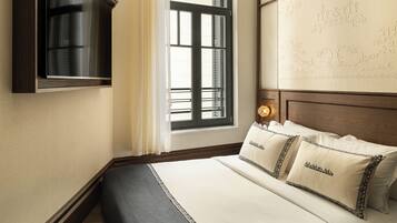 A hotel room with a bed, a TV mounted on the wall, a window with curtains, and a decorative headboard.