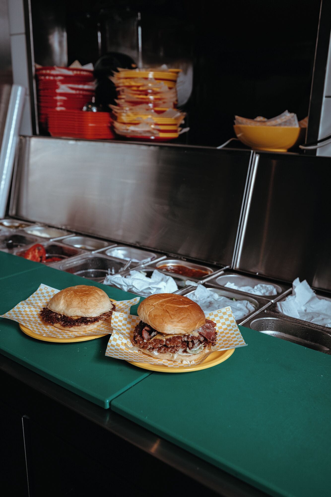 Deux sandwichs sur un comptoir vert, avec des récipients contenant des condiments en arrière-plan.