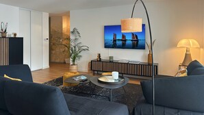 A modern living room with a flat-screen TV, a round coffee table, a sofa, and a lamp. - Spacious and elegant T4, city center (Vannes)