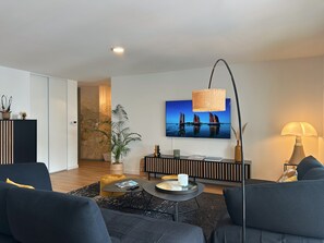 Ein modernes Wohnzimmer mit Flachbildfernseher, rundem Couchtisch, Sofa und einer Lampe.