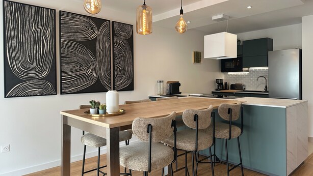 A modern kitchen with a central island, pendant lights, and abstract wall art. - Spacious and elegant T4, city center (Vannes)
