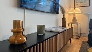 A modern living room with a TV mounted on the wall, a console table with decorative items, a lamp, and a framed picture. - Spacious and elegant T4, city center (Vannes)