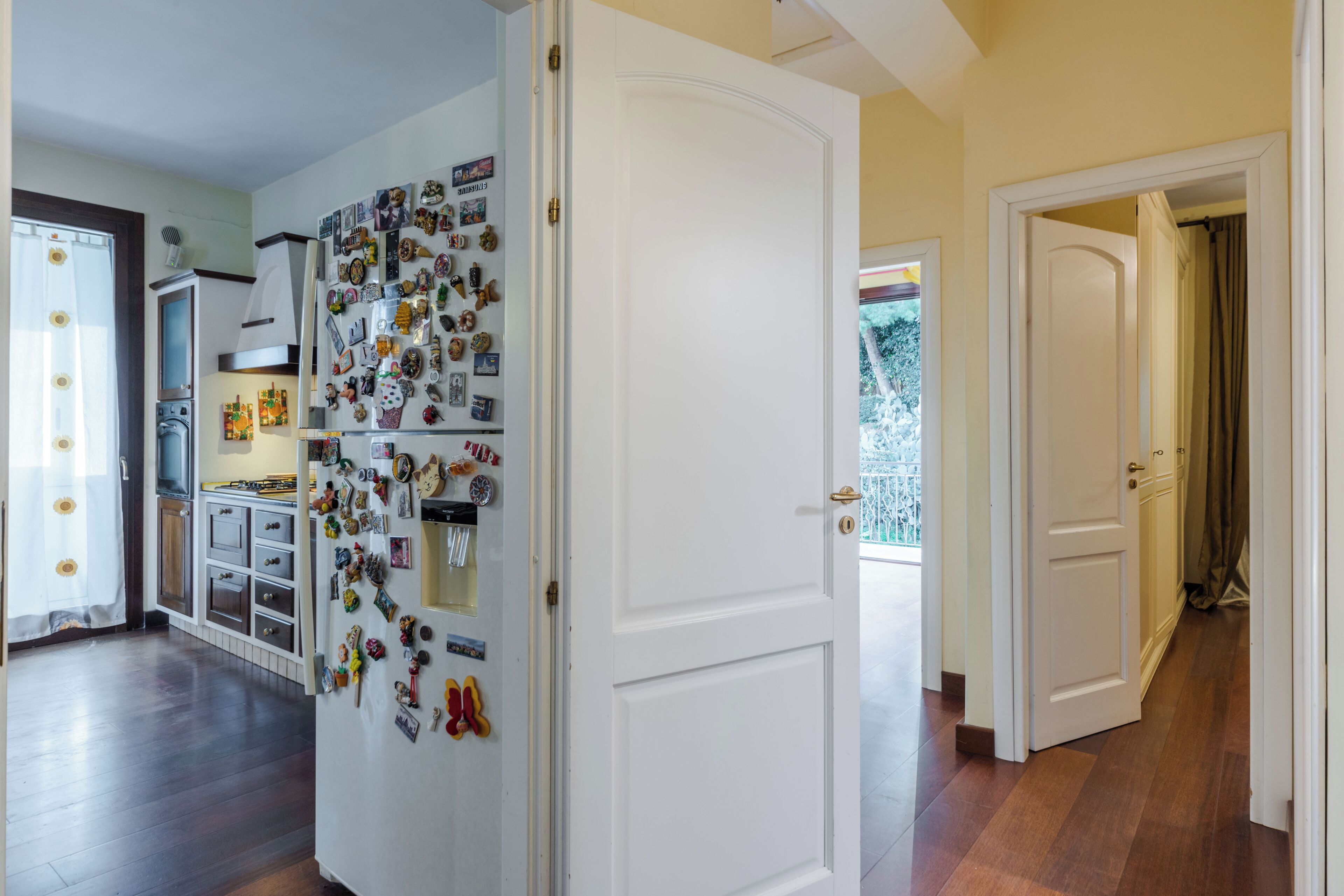 A kitchen with a refrigerator covered in magnets, a wooden cabinet, and a door leading to a balcony.