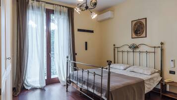A bedroom with a metal bed frame, a bedside table, a nightstand, a wall-mounted air conditioner, a framed picture, and a window with curtains.