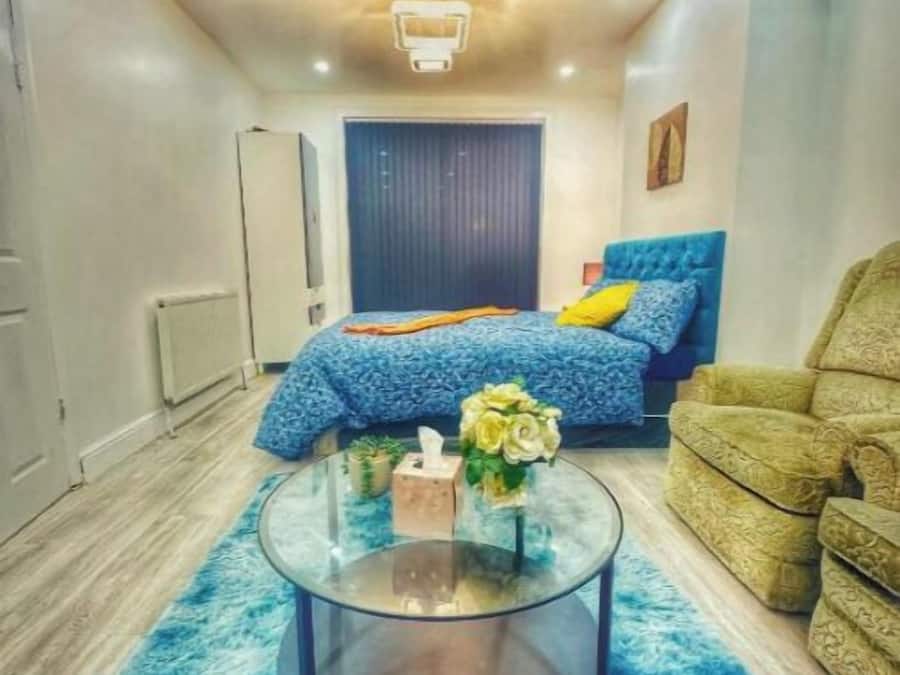 Un dormitorio moderno con una cama, una mesita de centro de cristal, una alfombra azul y un sillón verde.
