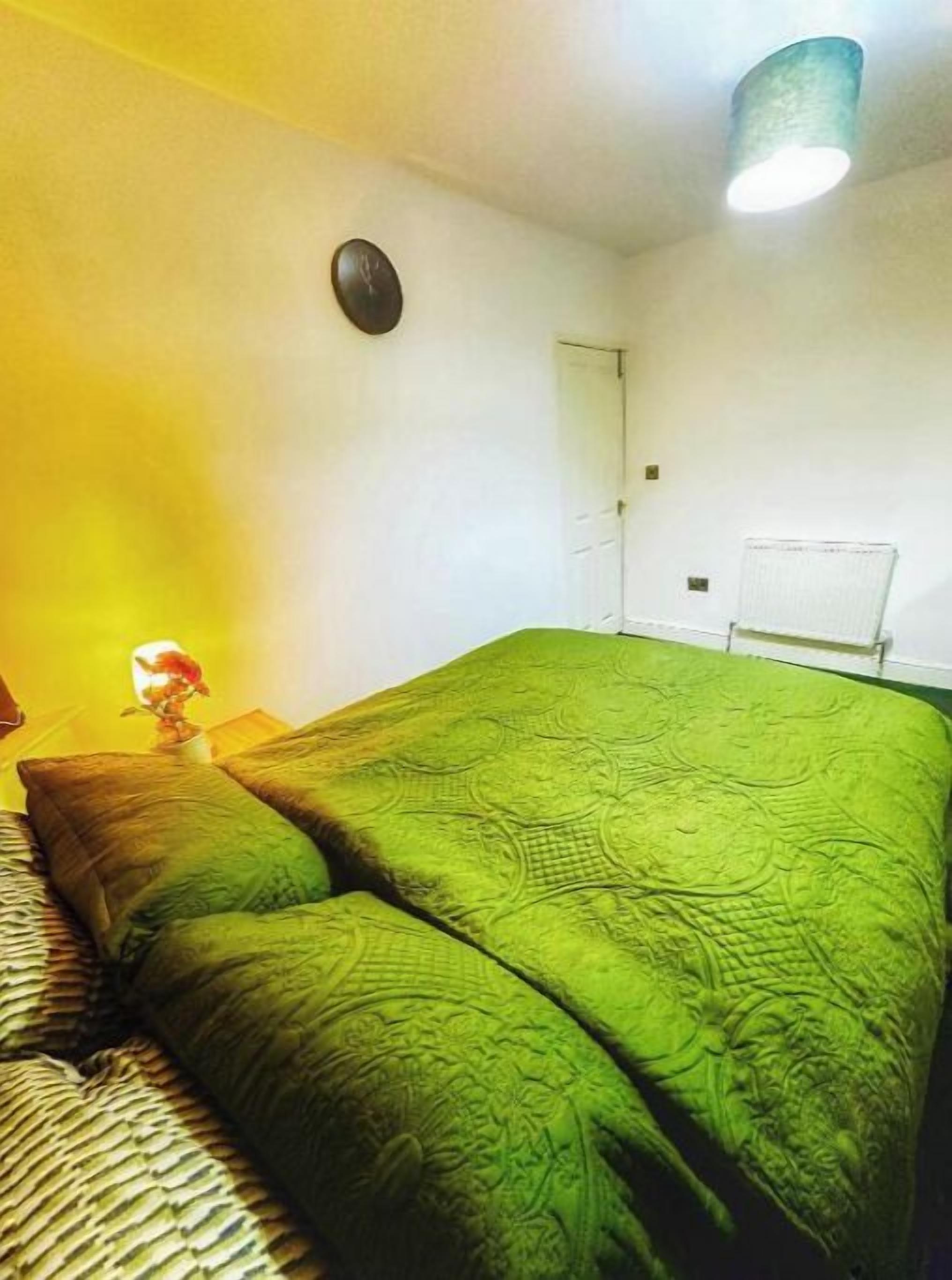 Et værelse med en seng, et natbord, en lampe, en dør og en radiator.