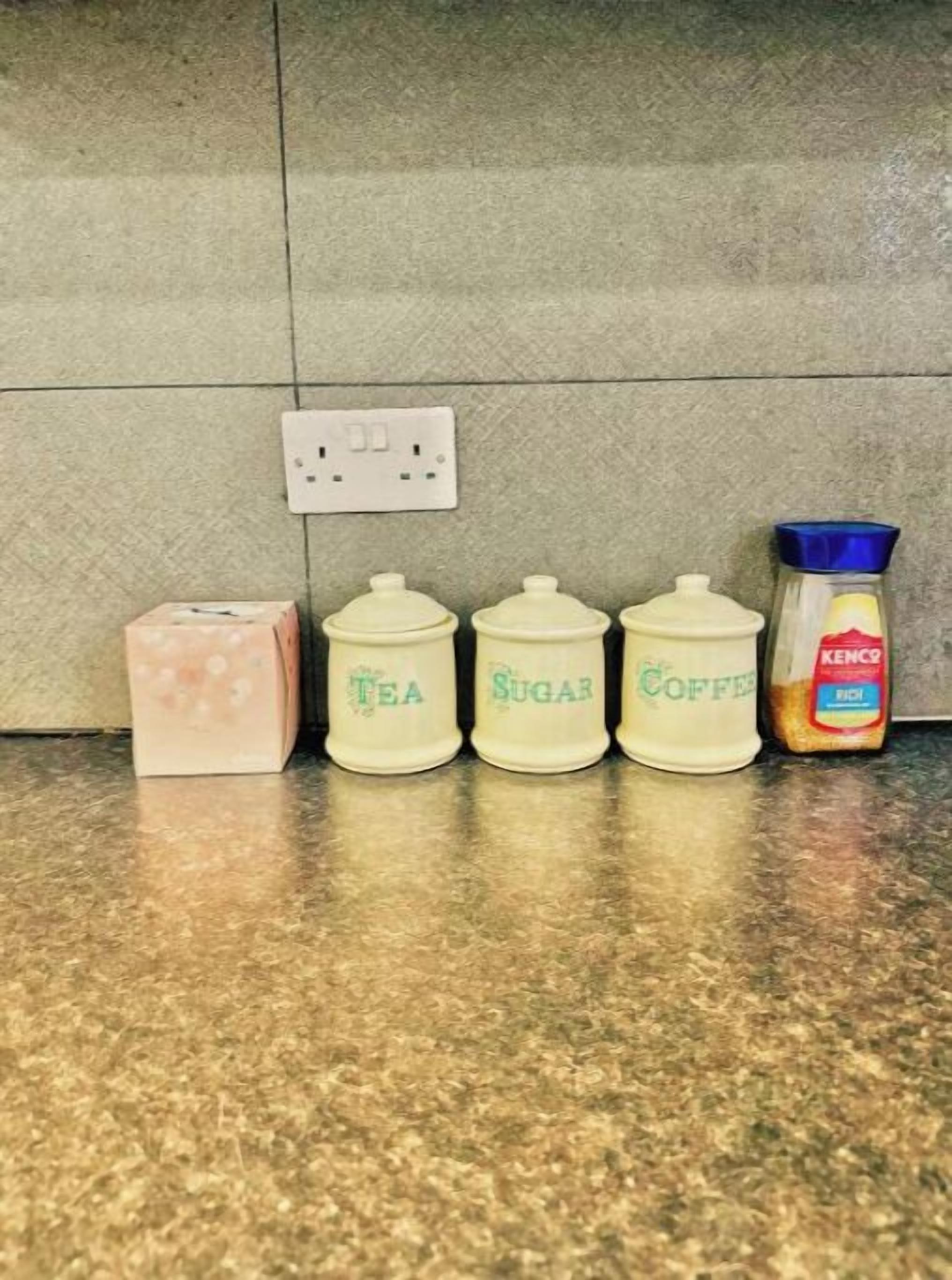 Una encimera de cocina con cuatro recipientes etiquetados como té, azúcar y café, y una caja de pañuelos.