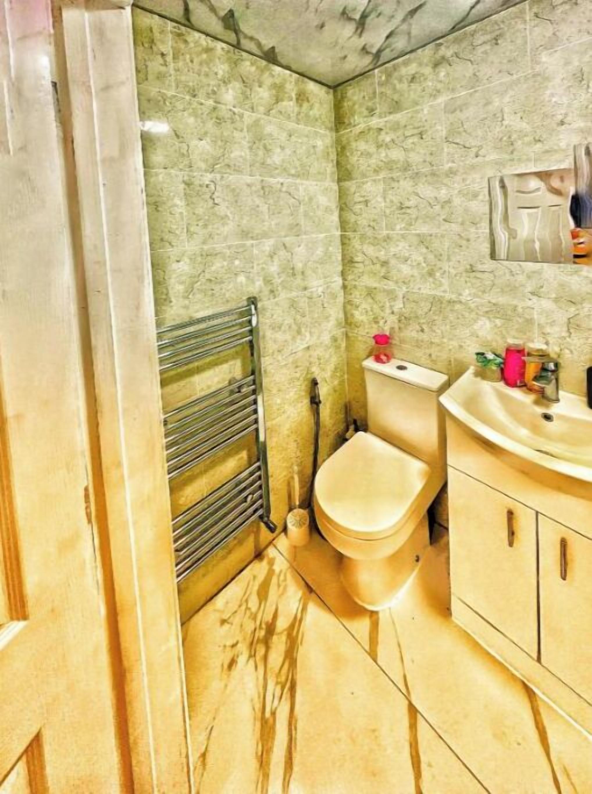 A bathroom with a marble floor, a toilet, a sink, and a towel rack.