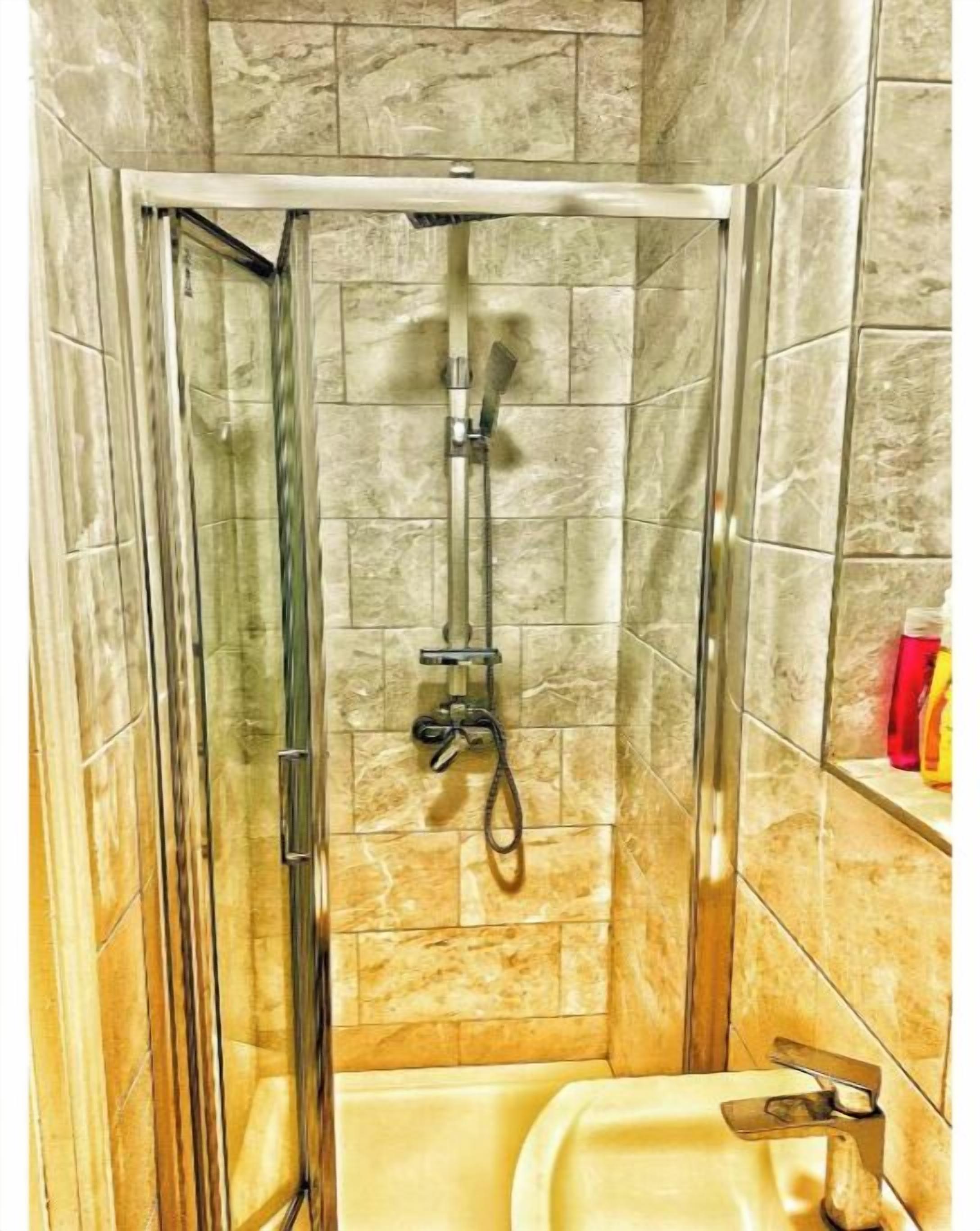 A shower stall with a glass door, a handheld showerhead, and a wall-mounted faucet.