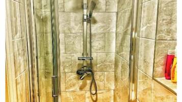 A shower stall with a glass door, a handheld showerhead, and a wall-mounted faucet.