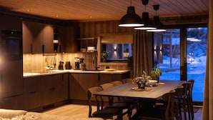 Una cocina moderna con armarios de madera, un comedor con mesa y sillas, y vistas a un paisaje nevado a través de amplios ventanales.