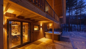 Una cabaña de madera con puerta de vidrio, un jacuzzi y un comedor.