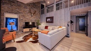 Una sala de estar moderna con una pared de piedra, una cabeza de ciervo montada, un televisor grande, un sofá y una chimenea.
