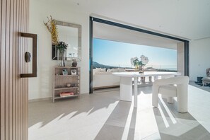 A modern interior with a white sofa, a round table, and a large window offering a view of the sea. - RLQ - Modern 2 Bed Apt With Rooftop Plunge Pool (Benahavis)