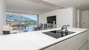 Ett modernt kök med en stor köksö, en matplats med stolar, en tv som är monterad på väggen och utsikt över bergen.