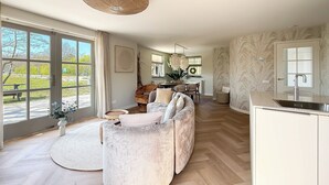 A spacious living area with a large window, a round rug, a sofa, and a kitchen with a modern sink. - Villa With Expansive Sunny Garden (Egmond aan den Hoef)