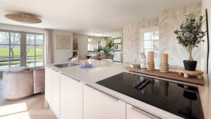 A modern kitchen with a large island, a dining area with chairs, and a view of the outdoors. - Villa With Expansive Sunny Garden (Egmond aan den Hoef)